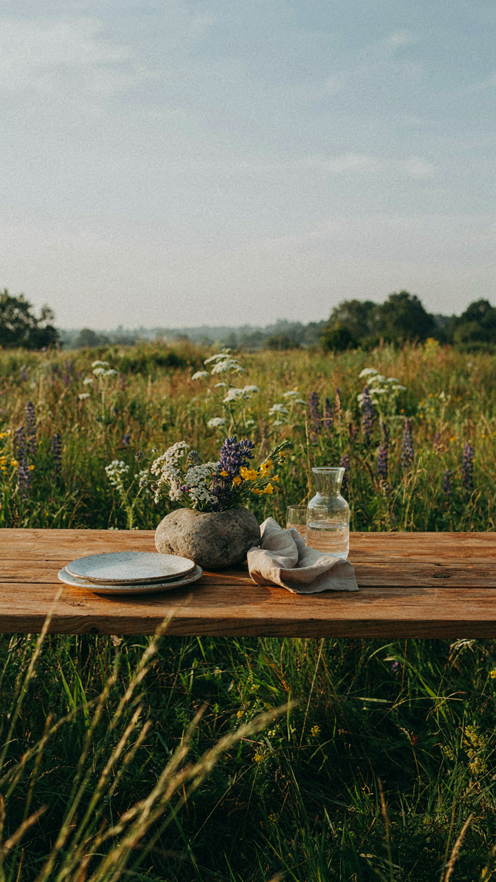 An elegant outdoor table setting made of natural wood and stone in a wild field.