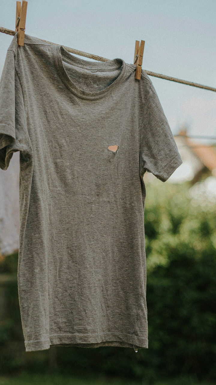 A worn out t-shirt with a small hole hanging on a clothesline.