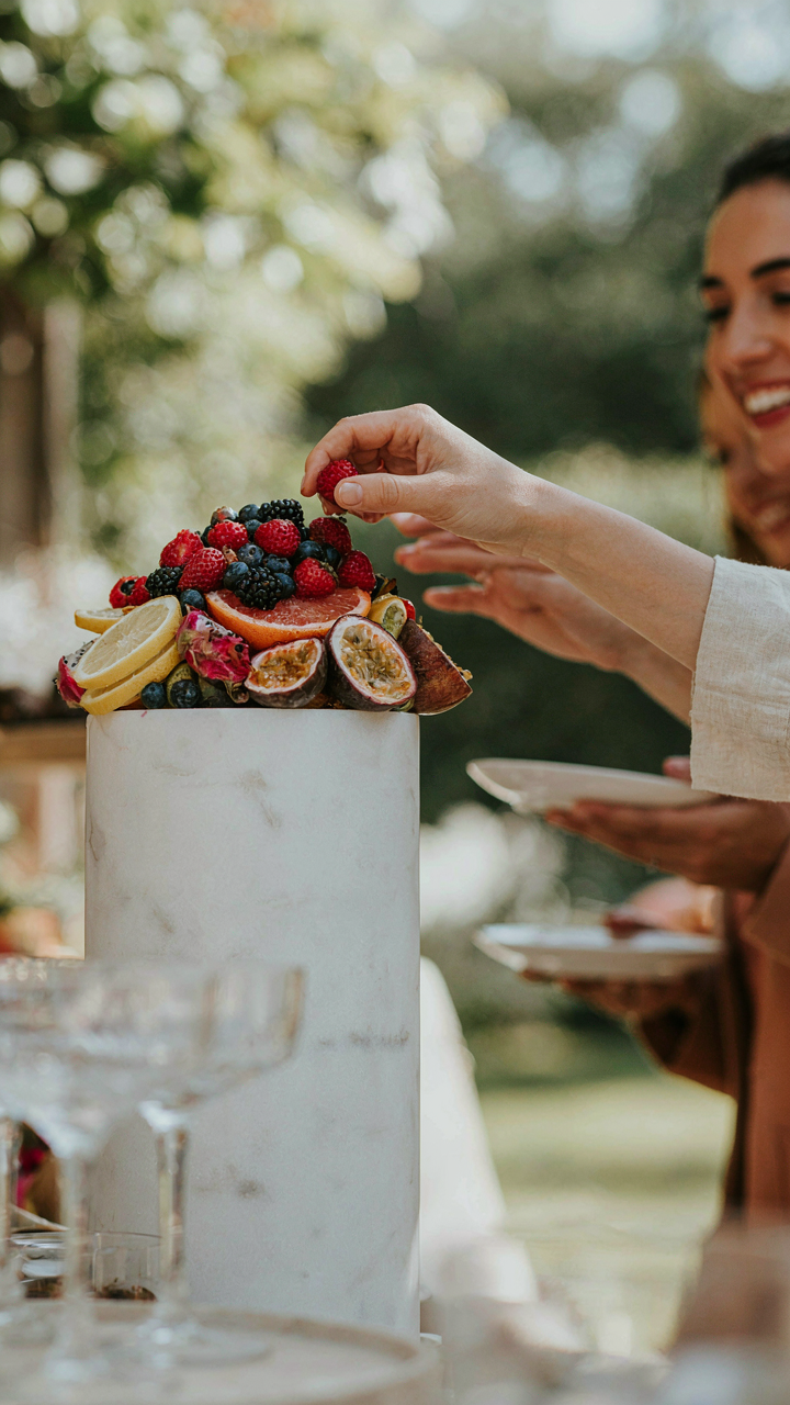 A stunning fruit arrangement on a pedestal with guests taking fruit.