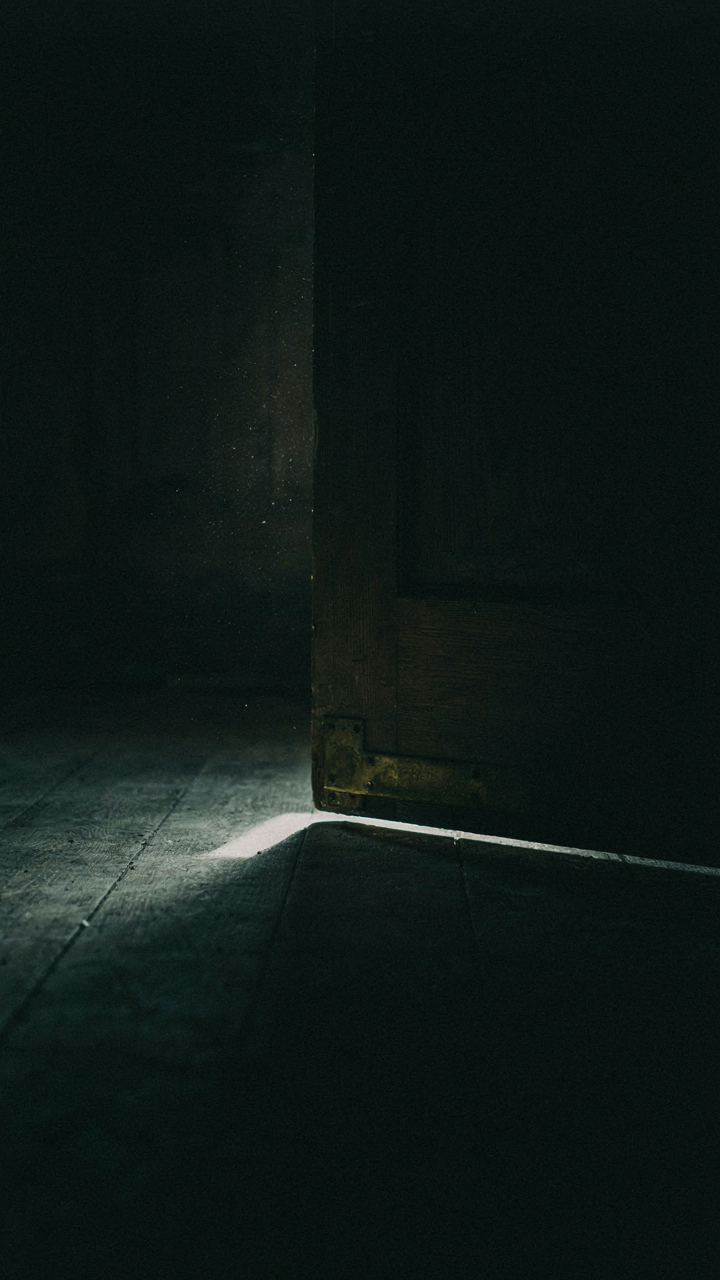 A very dark room with only a tiny bit of light coming from under a door.