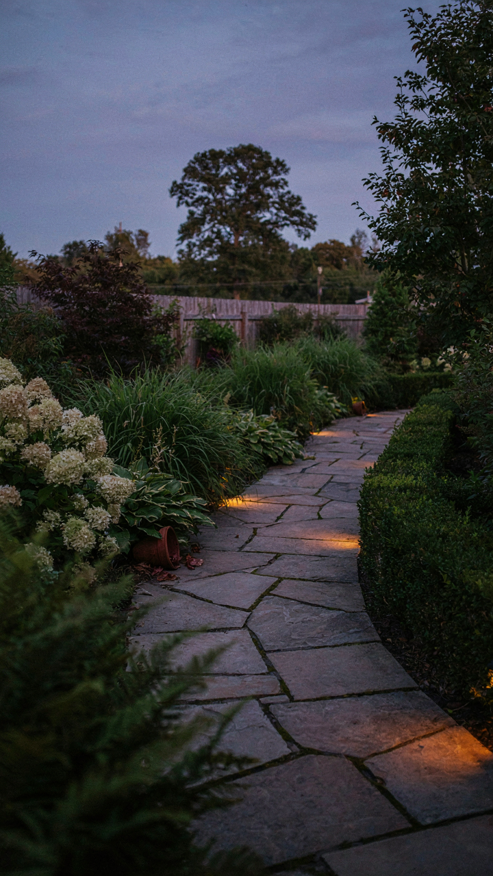 Soft ground lights create shadows and depth along a backyard path at night.