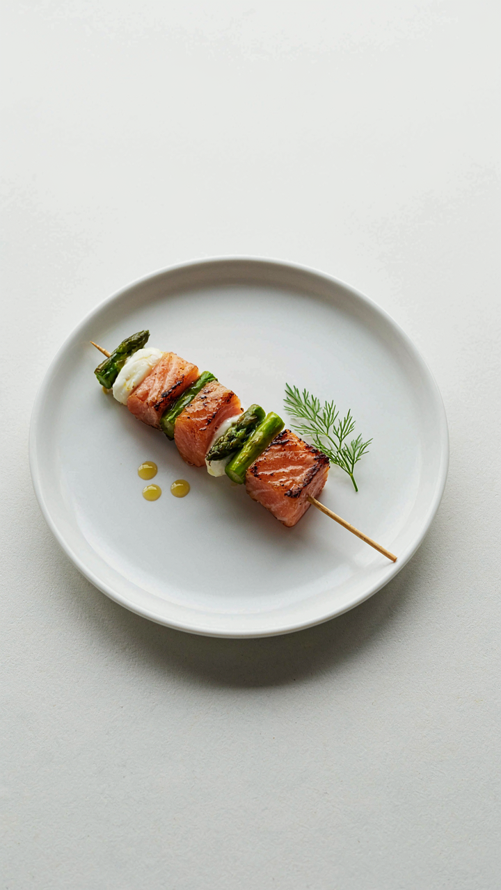 A minimalist single skewer appetizer on a white plate.