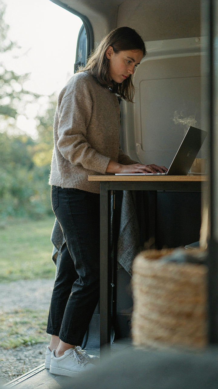 A person stands at a desk, working on a laptop inside a Sprinter van.