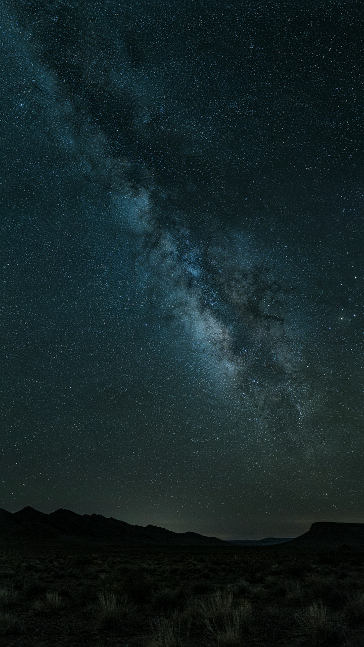 A clear night sky filled with many bright stars over a dark landscape.