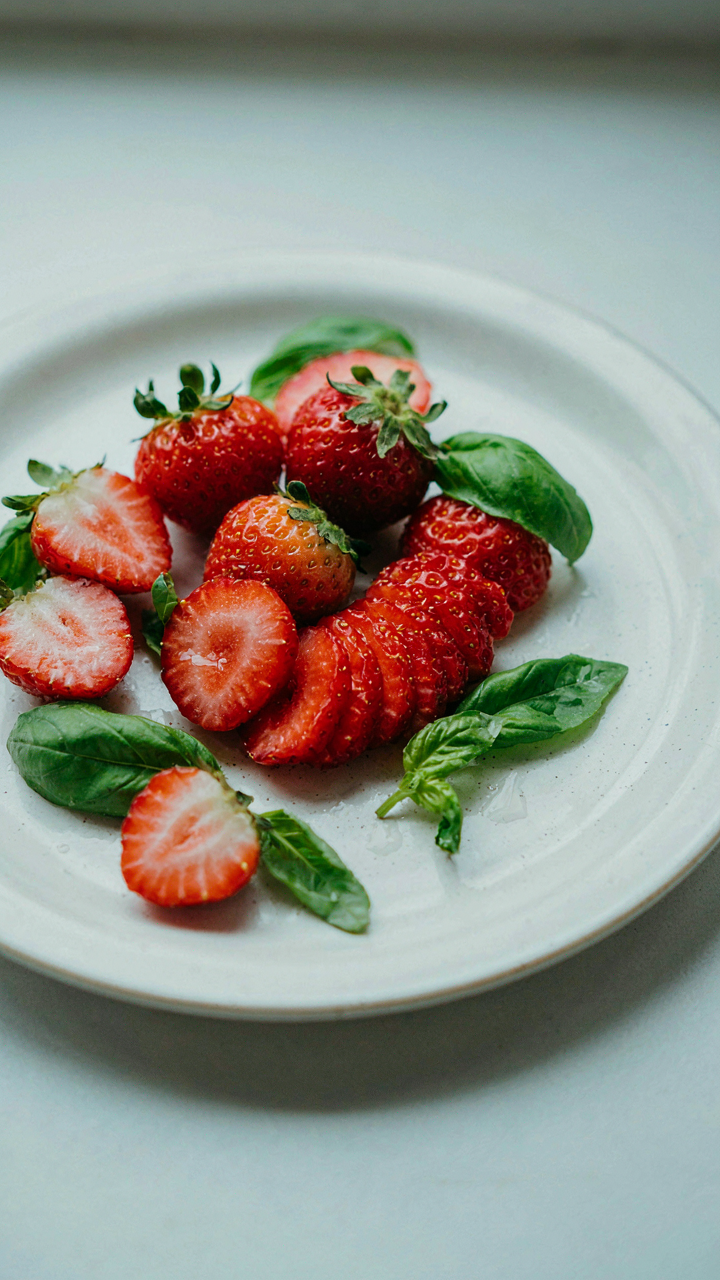 Sliced red strawberries are arranged next to fresh green basil leaves.