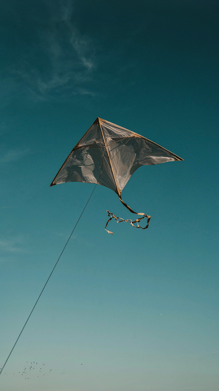 A large kite struggles against strong, uneven wind in a blue sky.