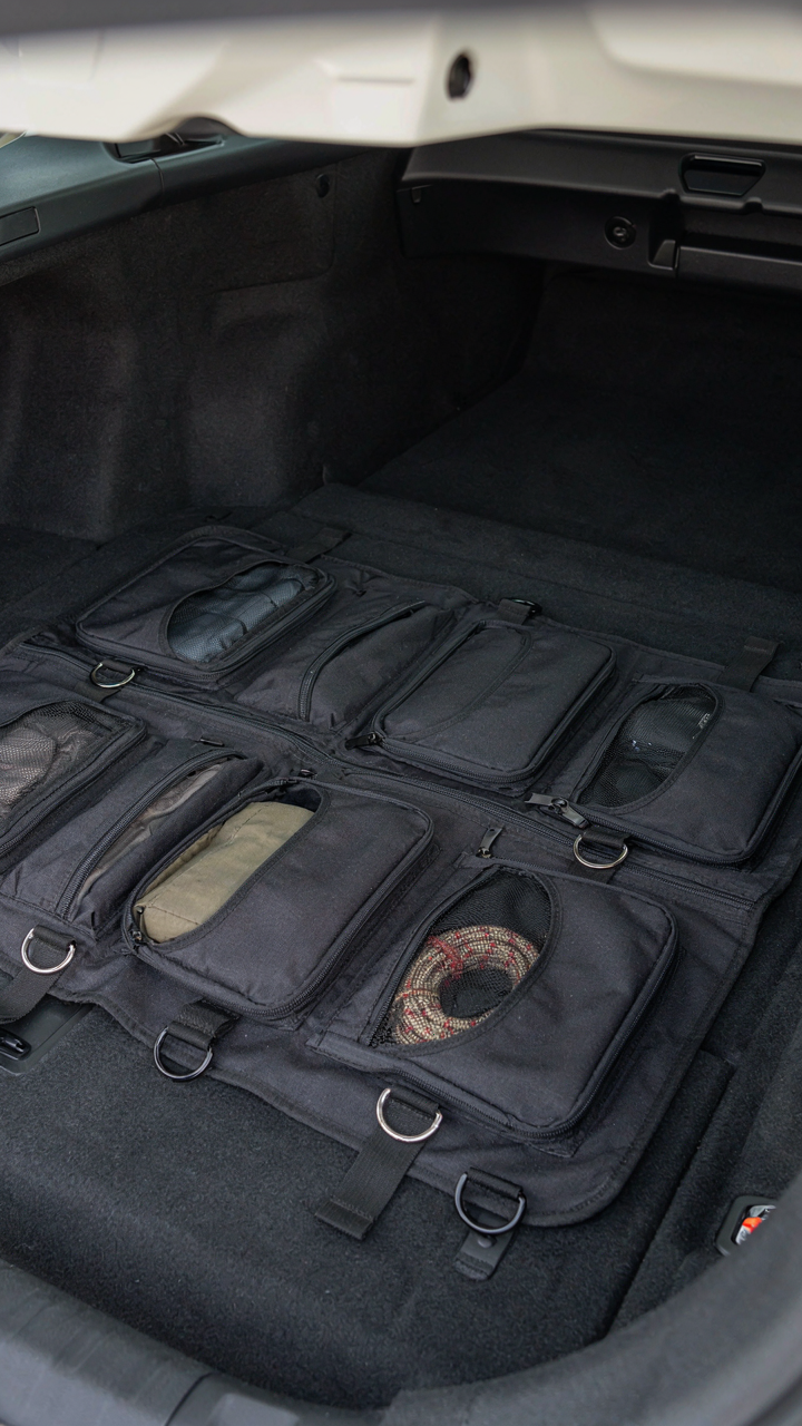An SUV trunk floor shows factory tie-down points anchoring a camping organizer.