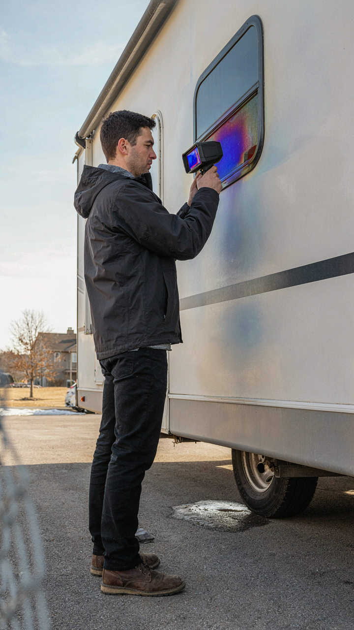 A person scans an RV exterior with a thermal camera to find heat loss.