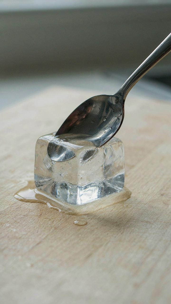 A hot metal spoon melts an ice cube quickly on a table.