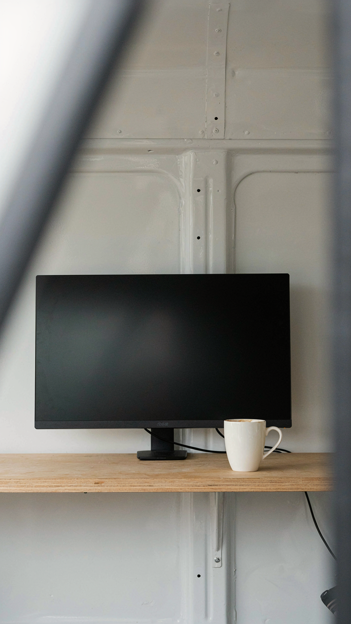 A single monitor sits on a wooden shelf in a tidy van life workspace.