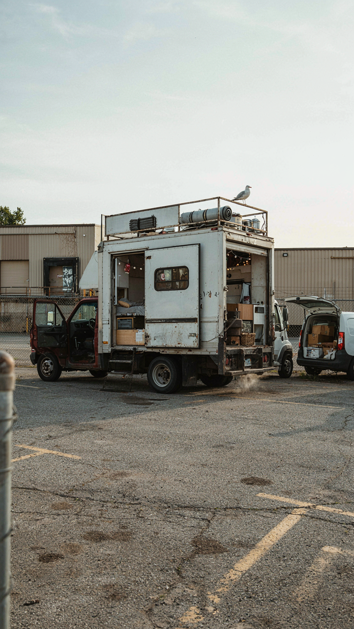 A box truck camper conversion is parked in a crowded, industrial parking lot.