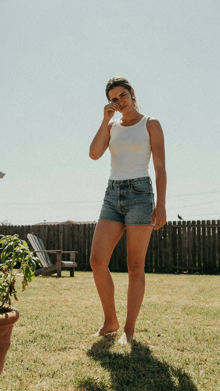 A person sweating in a sun-drenched backyard, looking for relief from the heat.