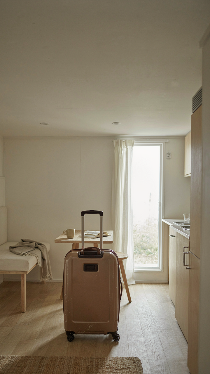 A small packed suitcase sits next to an empty, simple pop up camper inside.
