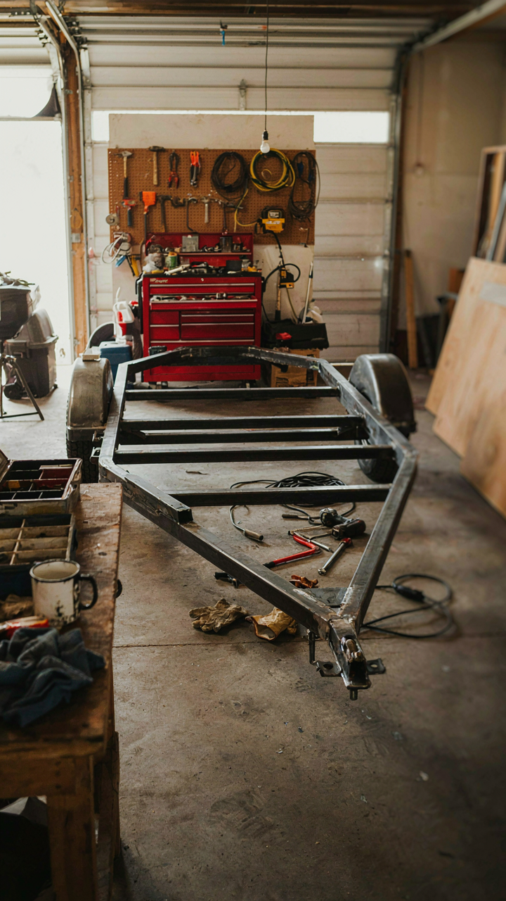 A partially built overland trailer frame in a messy garage.