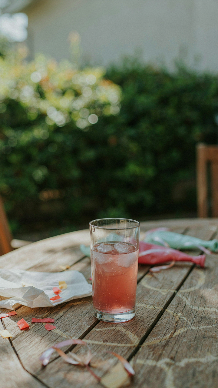 A lonely, diluted pink drink sits on a patio table with melted ice.