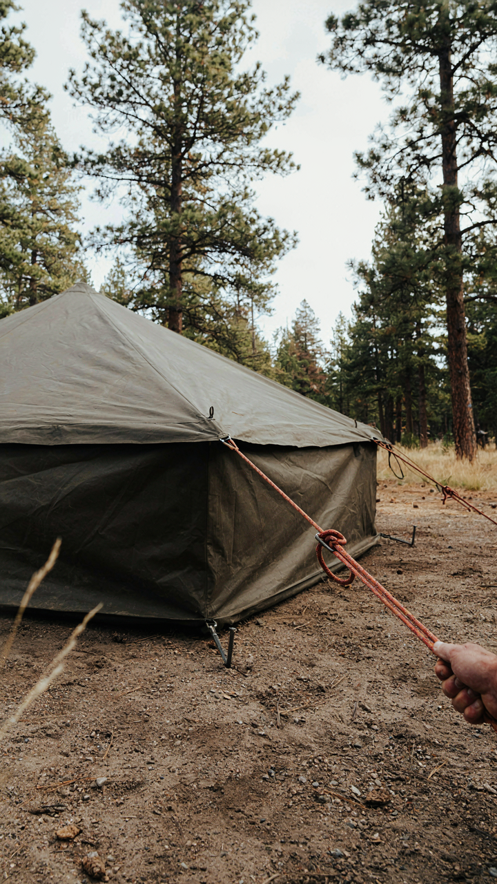 A large tent is securely anchored to the ground with strong ropes and stakes against wind.