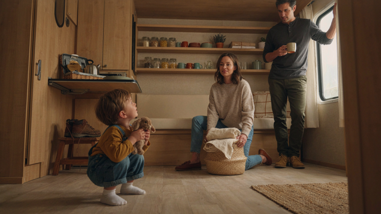 A small family smiles while organizing their cozy travel trailer with clever storage ideas.