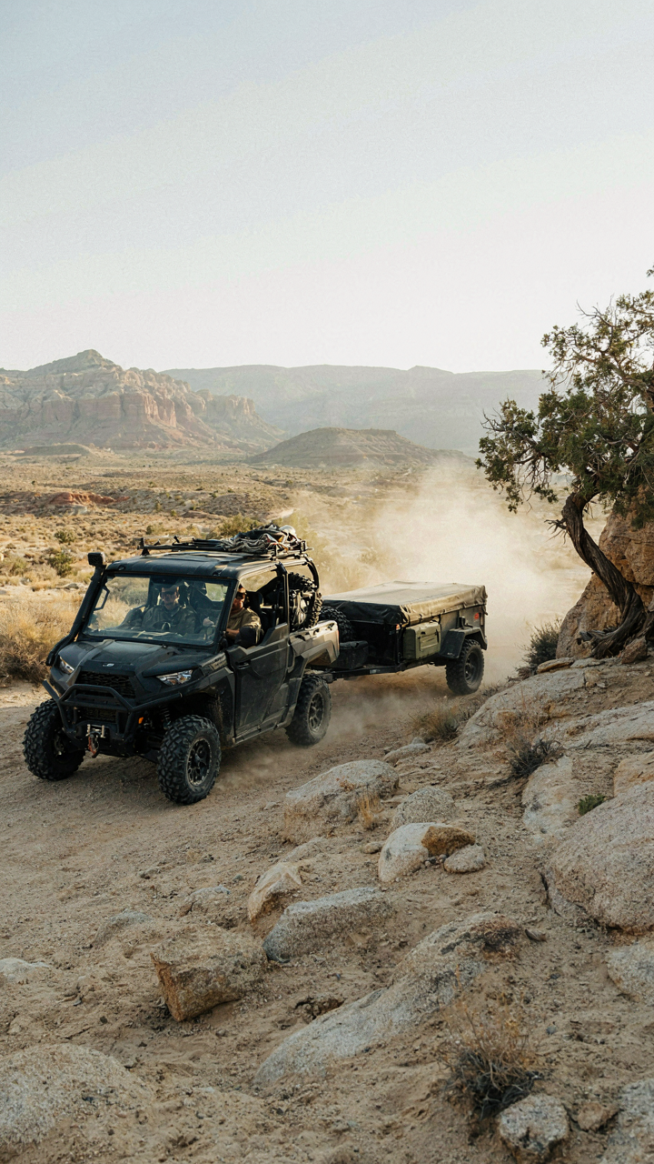 A UTV tows a small overland trailer on a rocky trail.