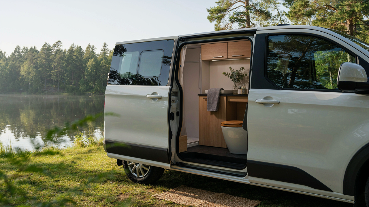 A modern camper van with an open side door, showing a small, clean van life bathroom.