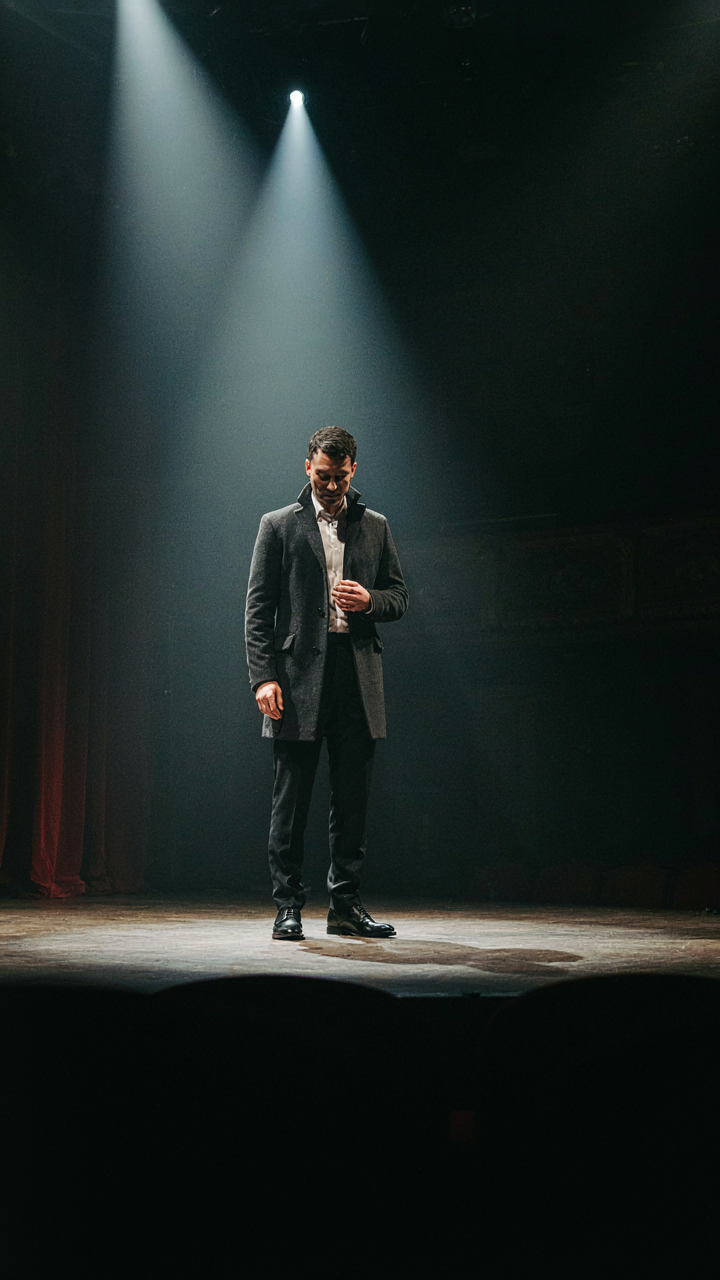 Bright stage lights illuminate an actor on a dark theater stage.