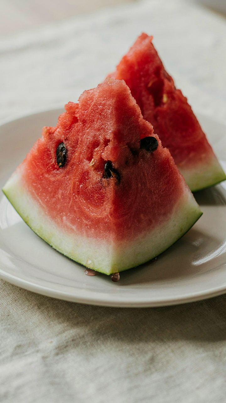 A bright red watermelon slice sits on a white plate.