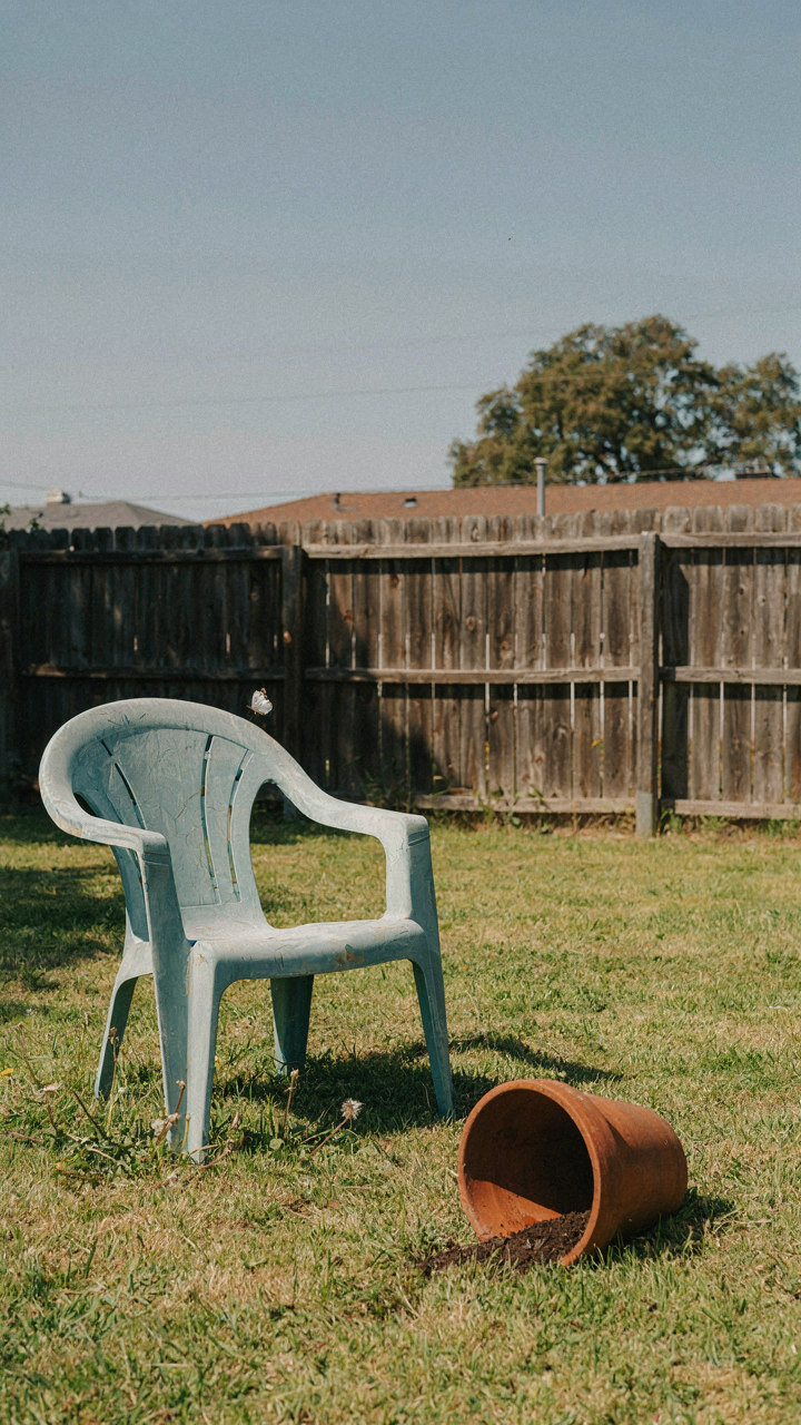 A faded, cracked plastic garden chair sits in a sunny backyard.