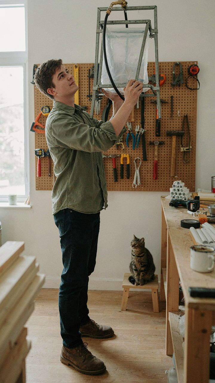 A person holds up a newly assembled diy camp shower in a workshop.