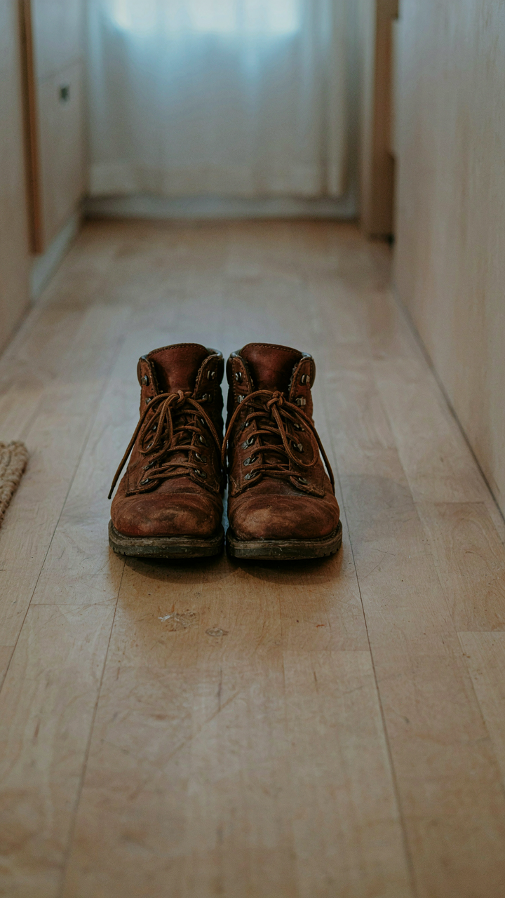 A single, worn pair of hiking boots rests on an empty floor inside a travel trailer.