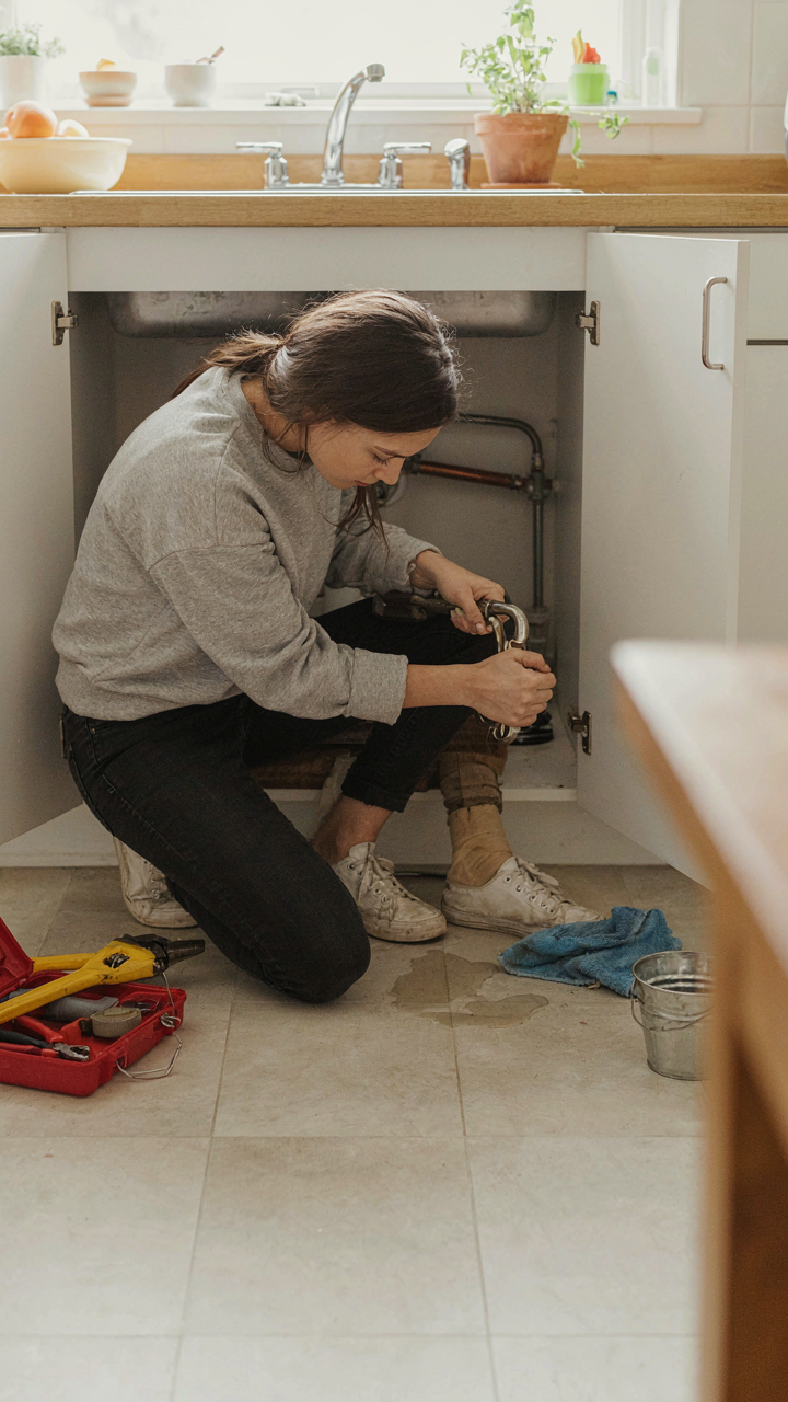 A person easily fixes a leaky pipe under a sink.