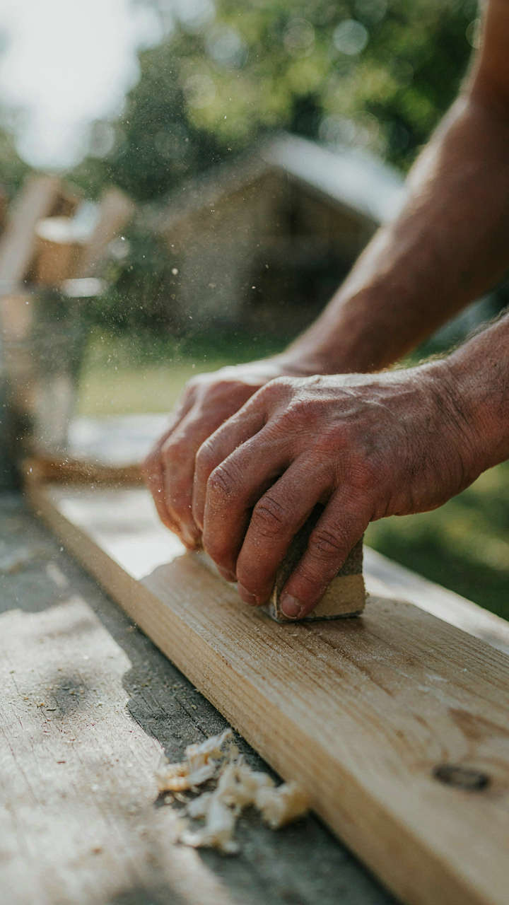 Hands diligently sanding a piece of raw lumber for a diy glamping setup.