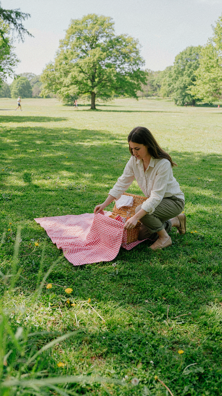 A determined person sets up a small picnic blanket and basket in a sunny park.