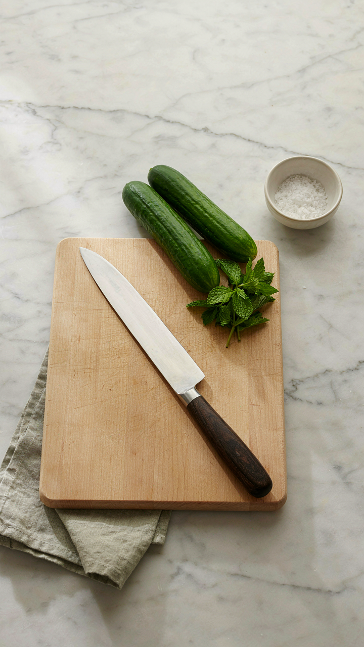 A chef's organized workstation with fresh cucumbers, mint, a cutting board, and a knife.