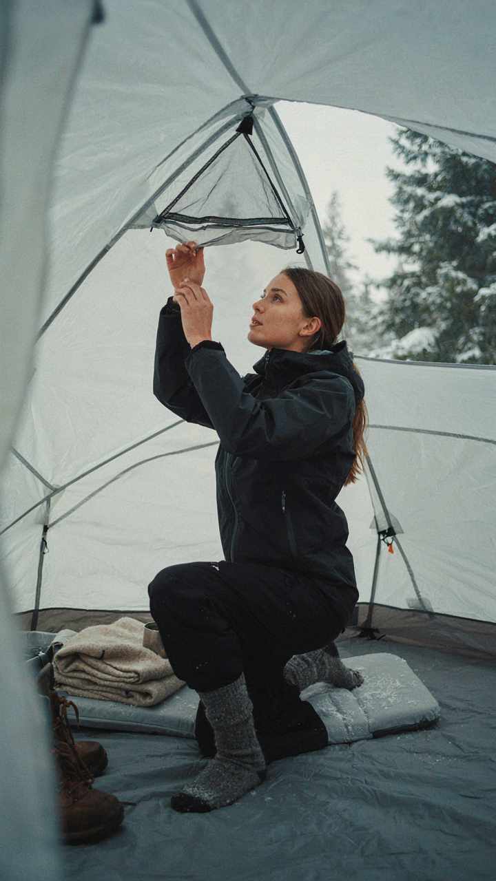 A person adjusts a tent flap in the snow.
